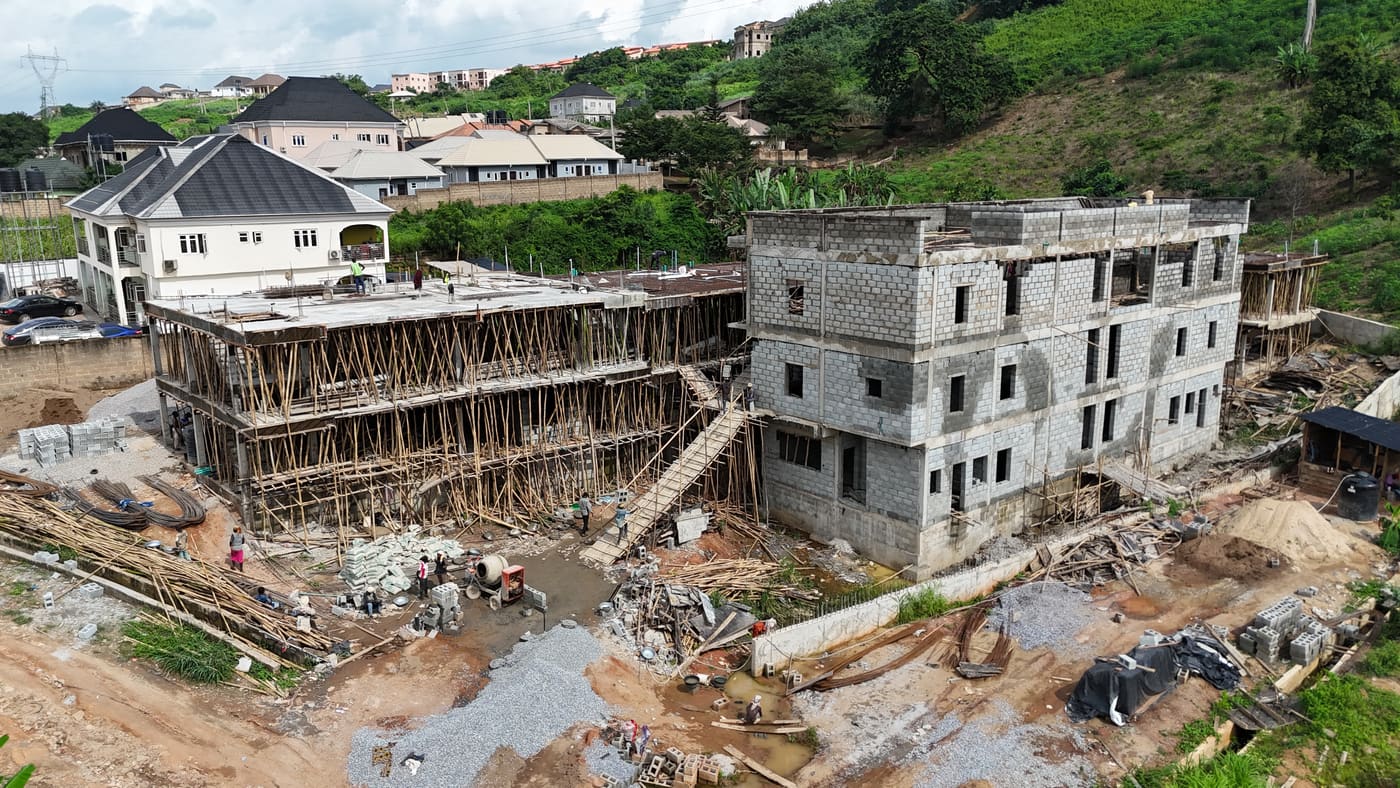 Ewang Estate under construction, 17 September 2025: blockwork risen through three storeys on the first block, bamboo scaffolding to full height, and a floor slab being cast on the block alongside. Aerial view 1 of 7.