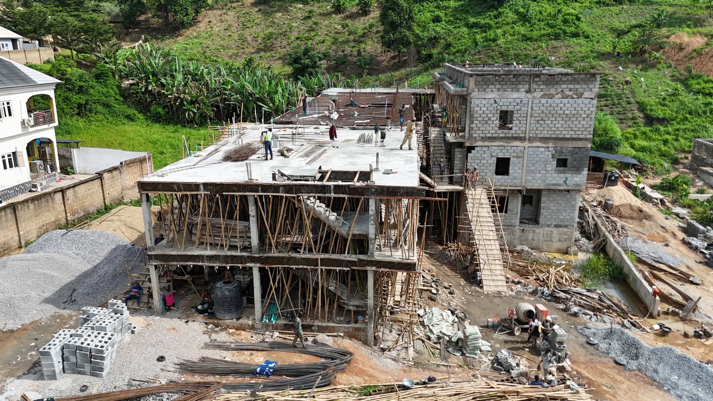 Ewang Estate under construction, 17 September 2025: blockwork risen through three storeys on the first block, bamboo scaffolding to full height, and a floor slab being cast on the block alongside. Aerial view 2 of 7.