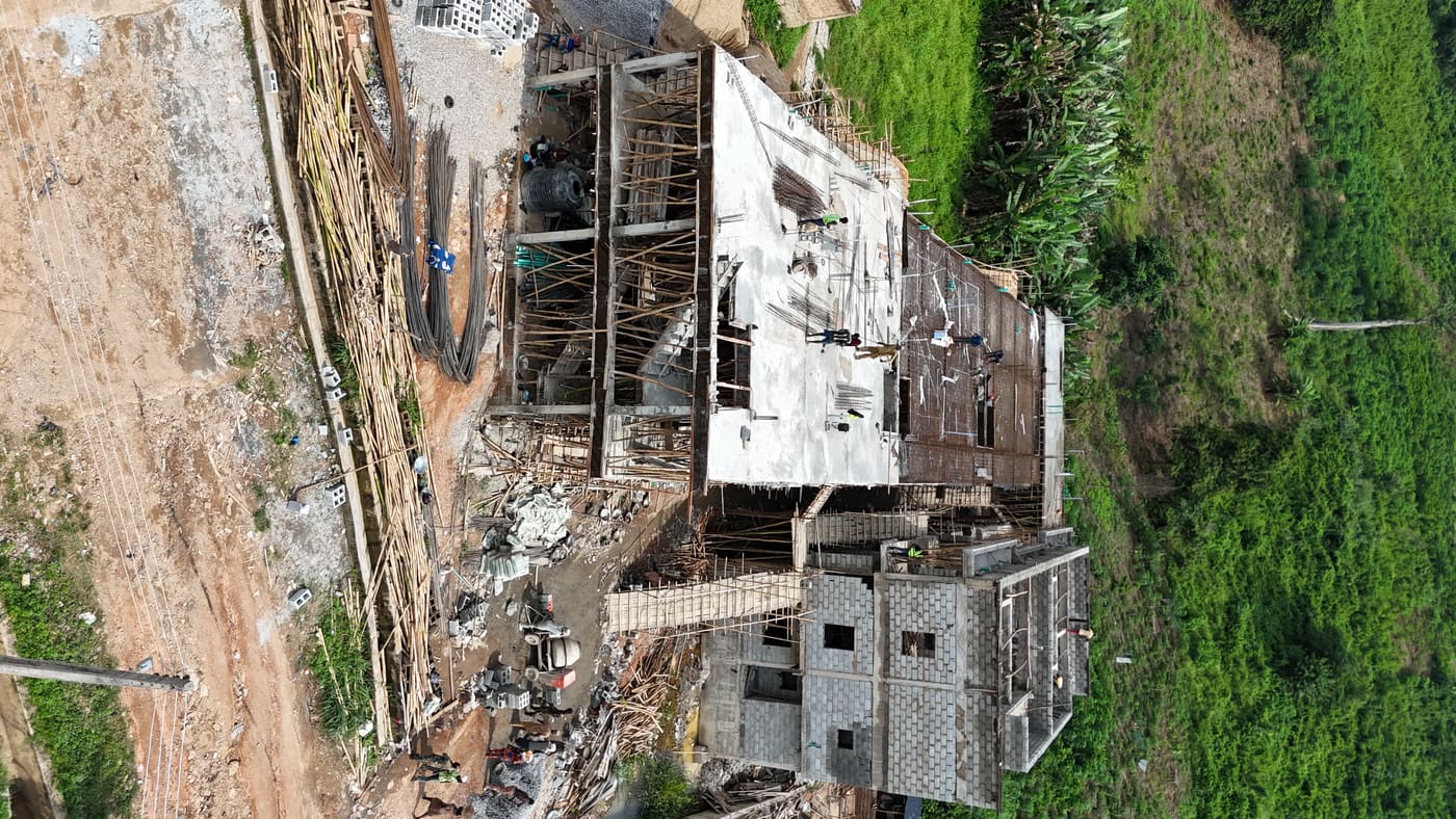 Ewang Estate under construction, 17 September 2025: blockwork risen through three storeys on the first block, bamboo scaffolding to full height, and a floor slab being cast on the block alongside. Aerial view 3 of 7.