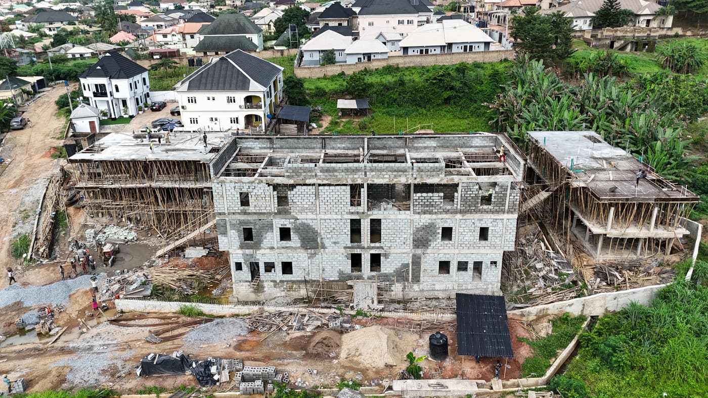Ewang Estate under construction, 17 September 2025: blockwork risen through three storeys on the first block, bamboo scaffolding to full height, and a floor slab being cast on the block alongside. Aerial view 4 of 7.