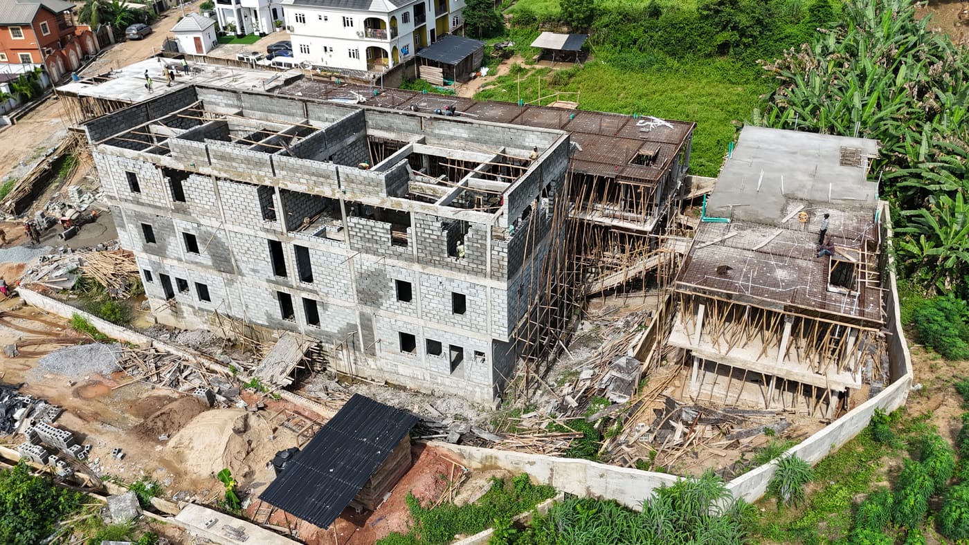 Ewang Estate under construction, 17 September 2025: blockwork risen through three storeys on the first block, bamboo scaffolding to full height, and a floor slab being cast on the block alongside. Aerial view 5 of 7.