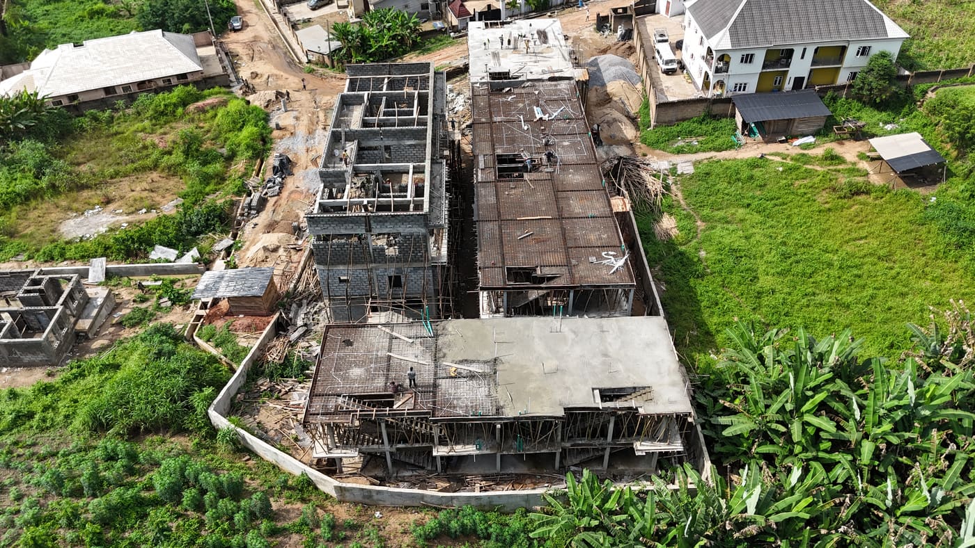 Ewang Estate under construction, 17 September 2025: blockwork risen through three storeys on the first block, bamboo scaffolding to full height, and a floor slab being cast on the block alongside. Aerial view 6 of 7.