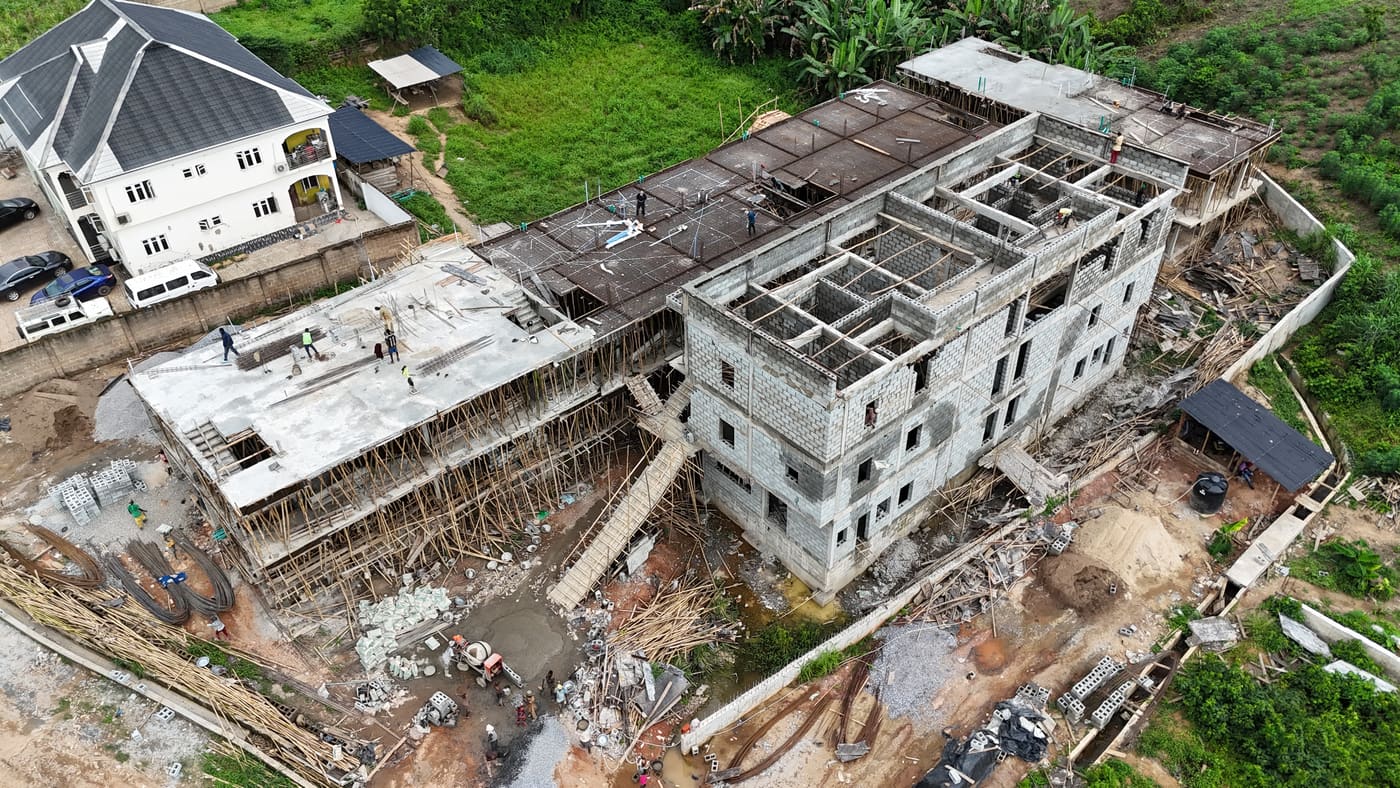 Ewang Estate under construction, 17 September 2025: blockwork risen through three storeys on the first block, bamboo scaffolding to full height, and a floor slab being cast on the block alongside. Aerial view 7 of 7.