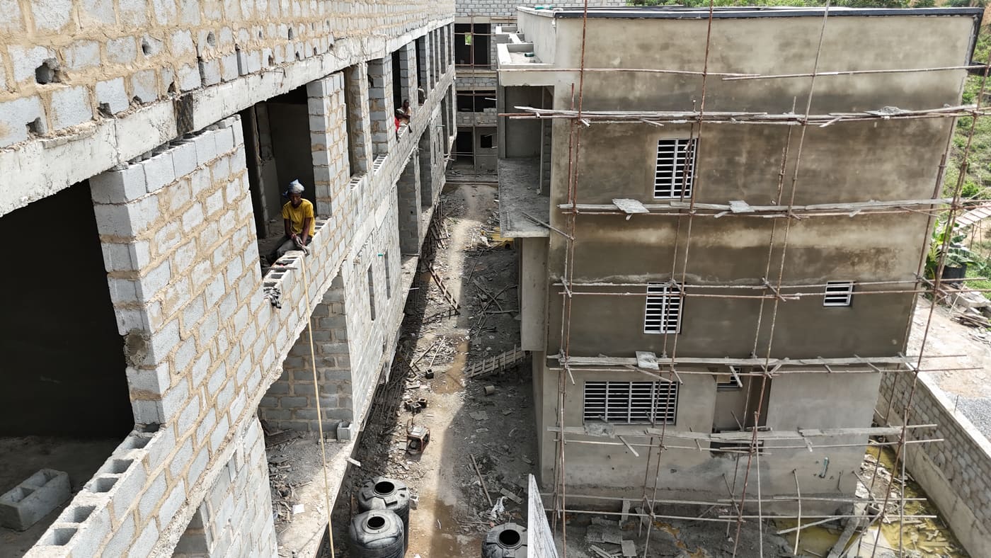 Ewang Estate under construction, 22 January 2026: blockwork complete across the blocks at three storeys, window and door openings formed, and the first render coats going on. Aerial view 2 of 7.