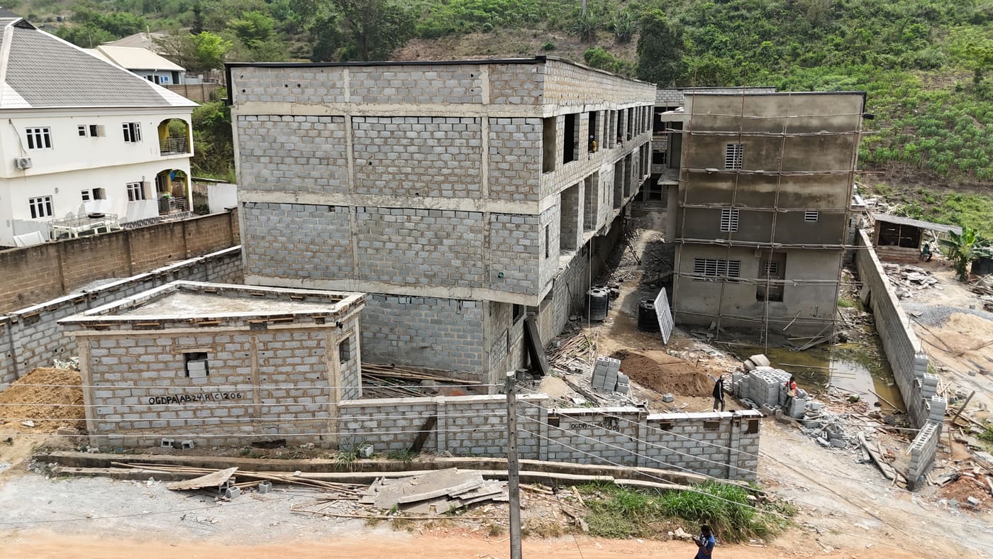 Ewang Estate under construction, 22 January 2026: blockwork complete across the blocks at three storeys, window and door openings formed, and the first render coats going on. Aerial view 3 of 7.