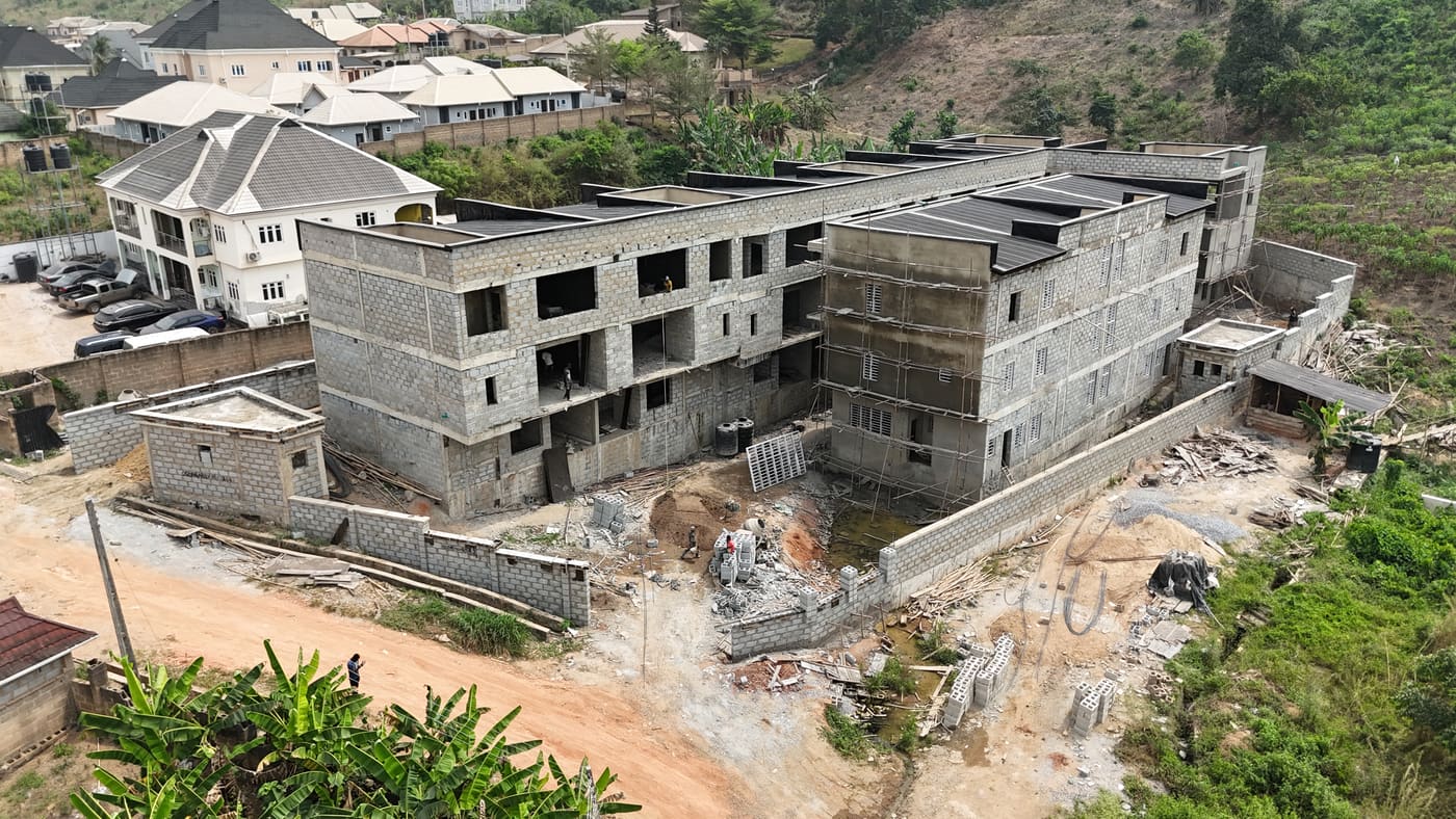 Ewang Estate under construction, 22 January 2026: blockwork complete across the blocks at three storeys, window and door openings formed, and the first render coats going on. Aerial view 4 of 7.