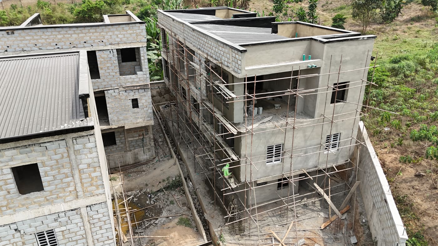 Ewang Estate under construction, 22 January 2026: blockwork complete across the blocks at three storeys, window and door openings formed, and the first render coats going on. Aerial view 5 of 7.