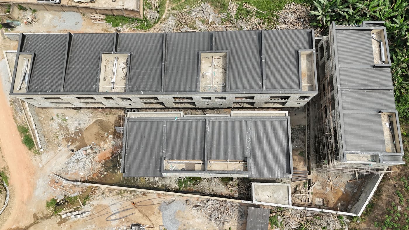 Ewang Estate under construction, 22 January 2026: blockwork complete across the blocks at three storeys, window and door openings formed, and the first render coats going on. Aerial view 6 of 7.