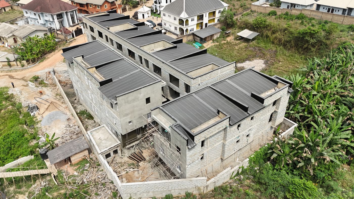 Ewang Estate under construction, 22 January 2026: blockwork complete across the blocks at three storeys, window and door openings formed, and the first render coats going on. Aerial view 7 of 7.