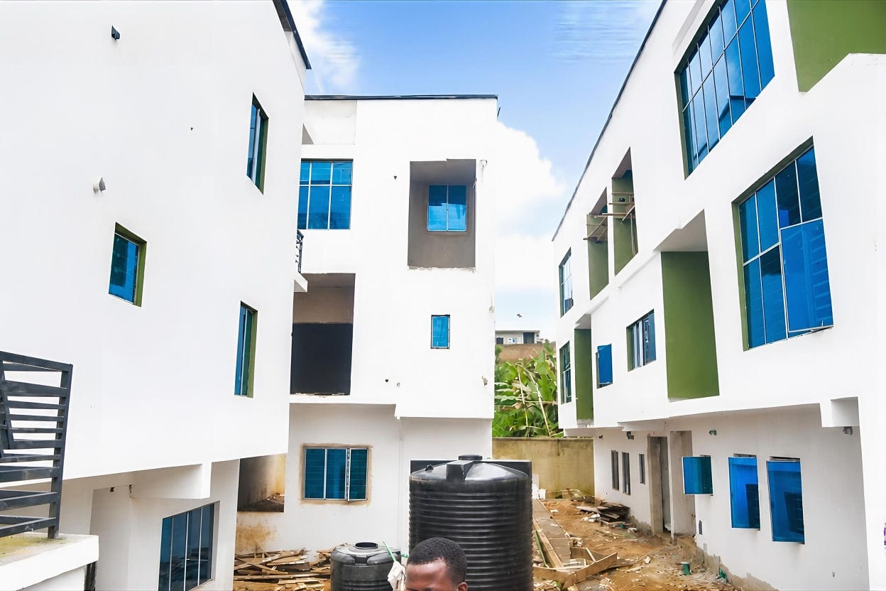 The courtyard between two blocks, rendered and painted, with reflective glazing fitted and black water storage tanks standing at ground level.