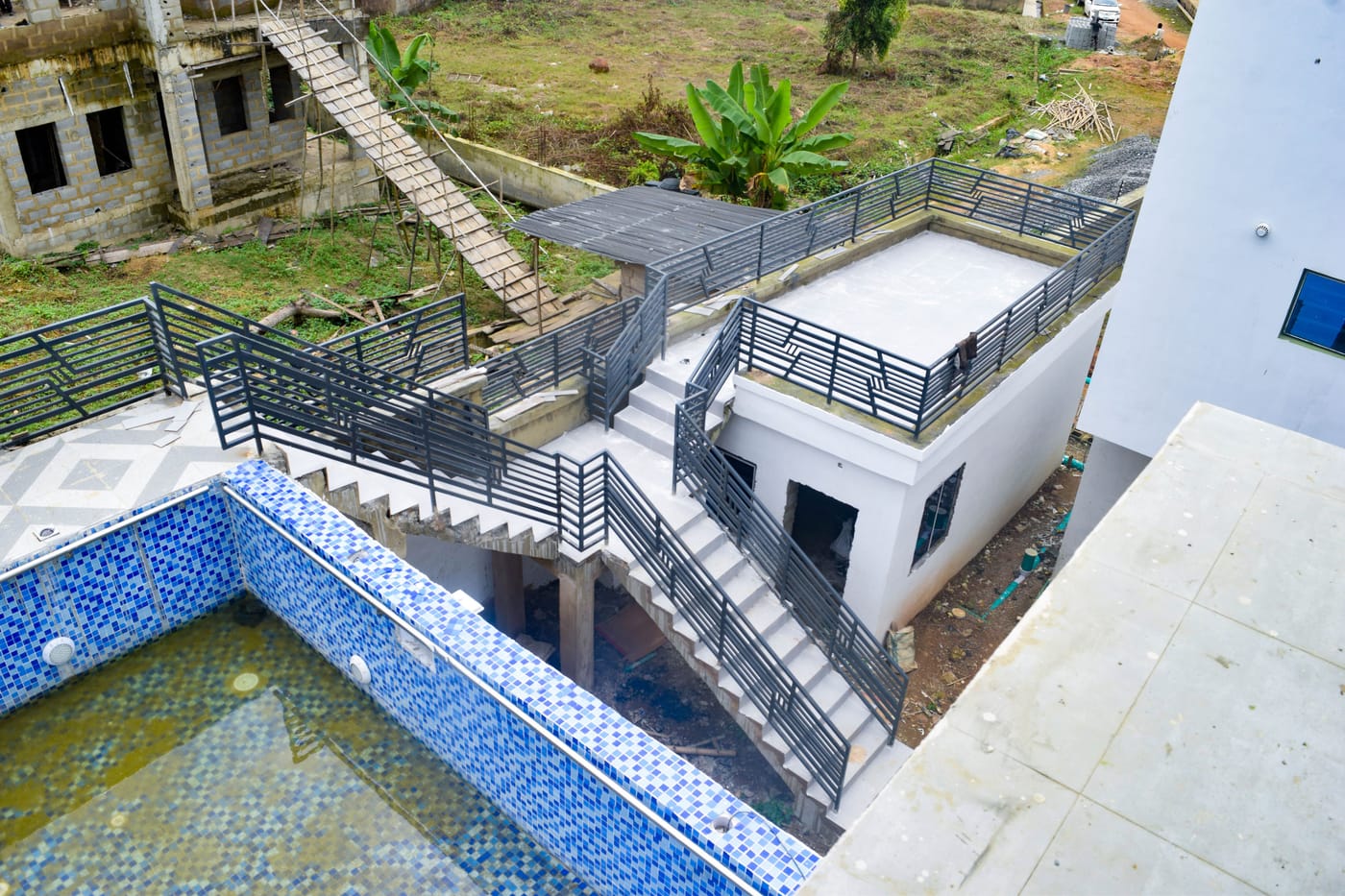 The swimming pool complete: blue mosaic tiling, filled with water, with the paved pool terrace, metal balustrades and the rendered plant room alongside.