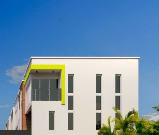 Street-level view of an apartment block at Ewang Estate against a clear sky, showing the lime-framed upper balcony and slim vertical windows.